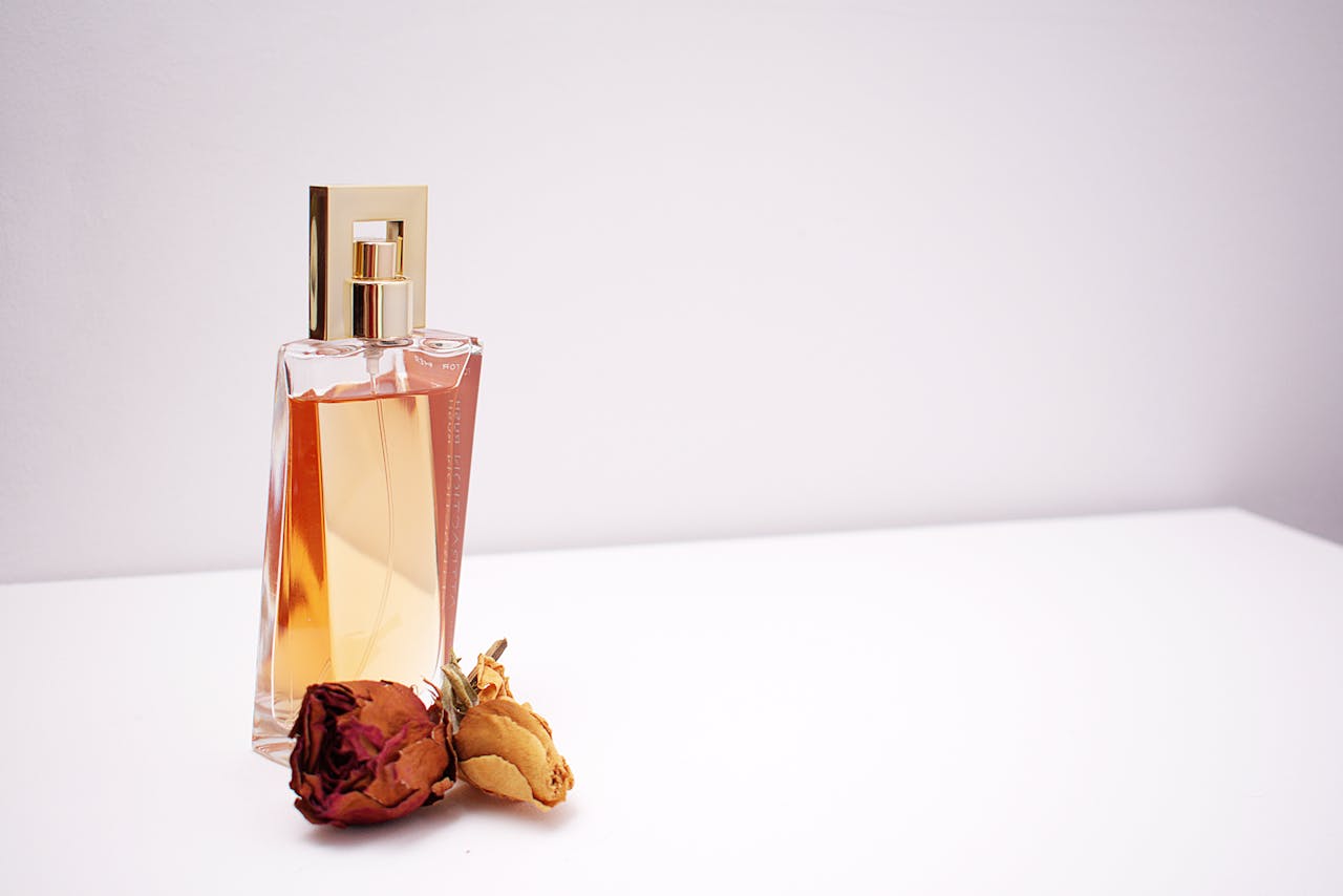 creative-03 Elegant glass perfume bottle with luxurious design placed next to dried flowers against a minimalistic white background.