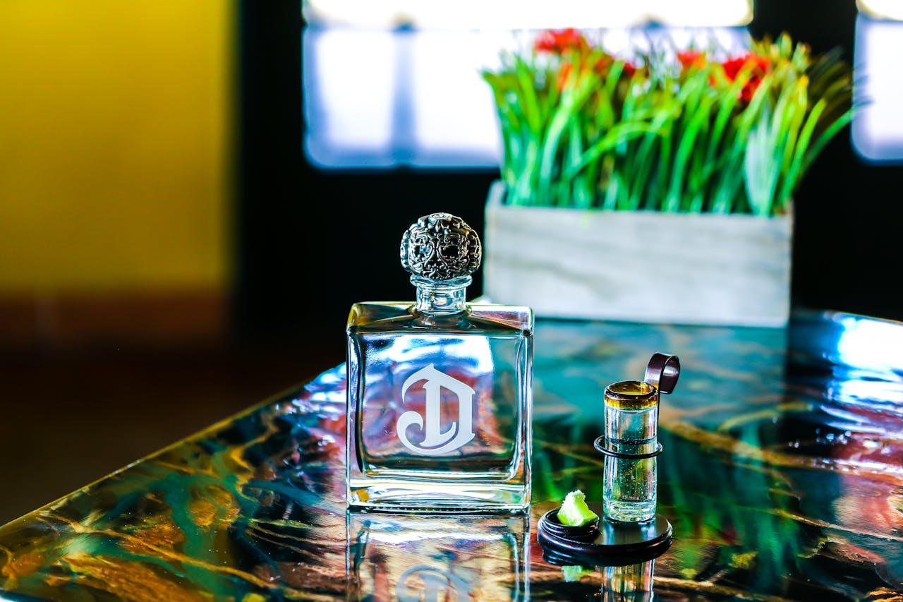 why-choose-us Close-up of a luxurious perfume bottle with a decorative cap on a colorful table with plants in the background.