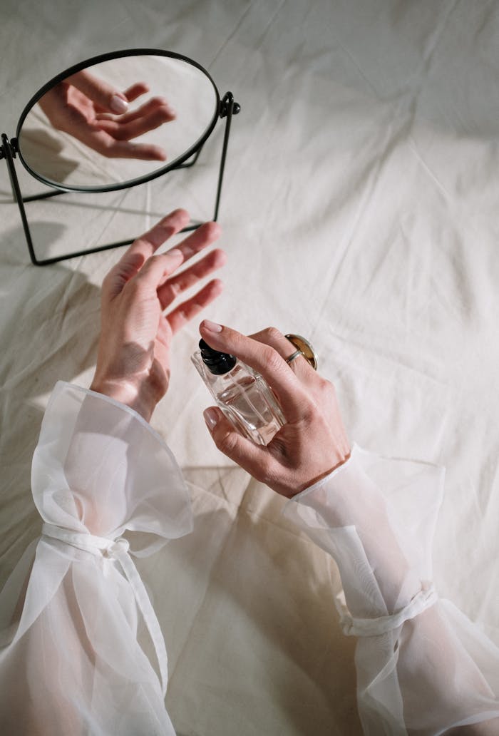 digital Hands in elegant sheer fabric holding perfume bottle near mirror, creating a graceful reflection.